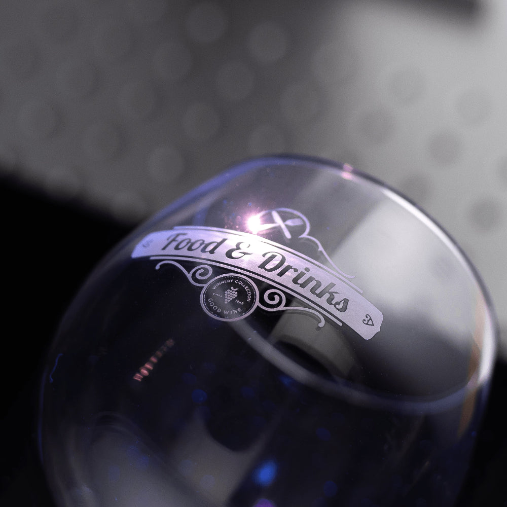 Close-up of a wine glass engraved with a UV laser with a brand label on a dark background