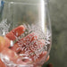 Clear glass with white floral pattern engraved with UV laser held by a hand against a blurred background